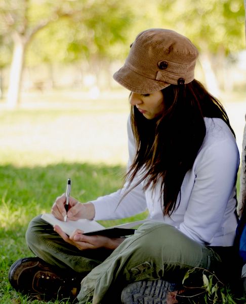 A human sitting in the grass writes in a journal.