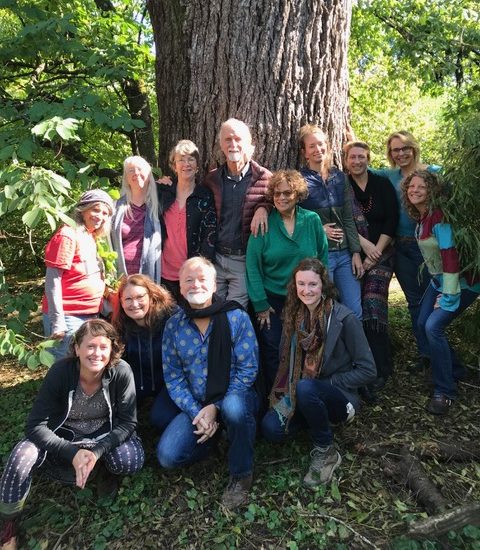 A group of smiling humans gathered in front of the trunk of a large tree.